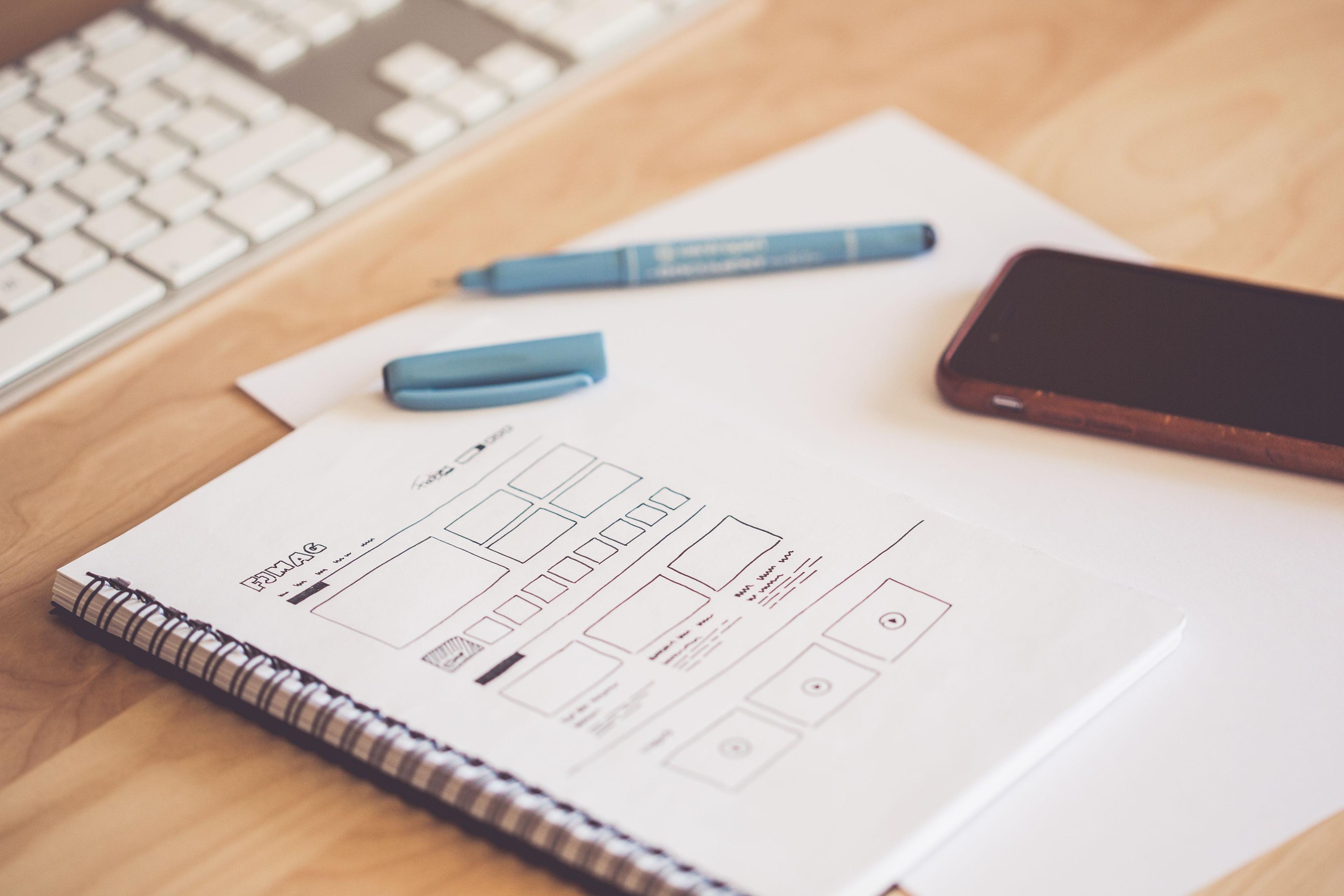 Sketchpad with wireframes and a smartphone on a wooden desk