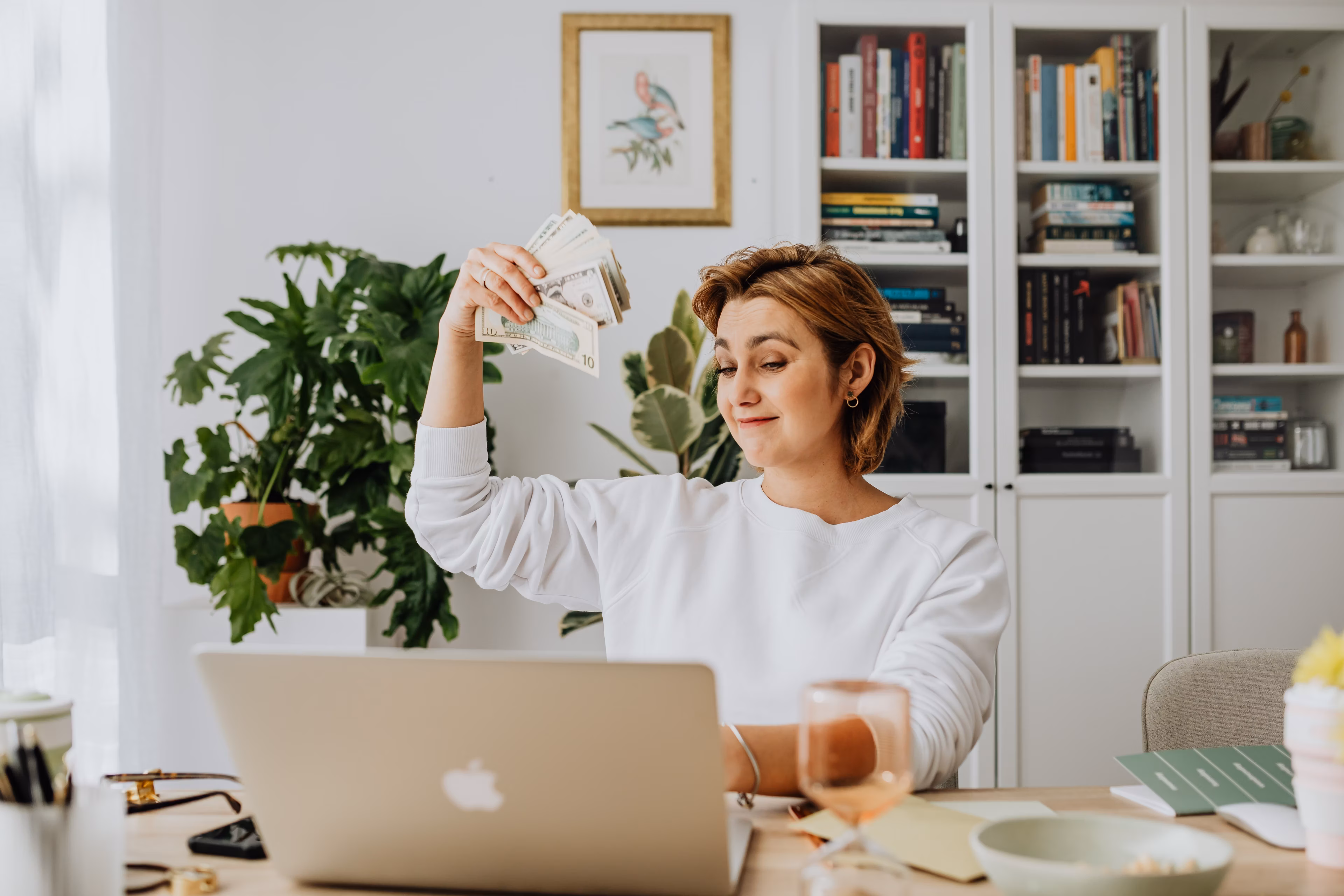 Woman sitting in an office in front of a laptop gesturing with cash in hand