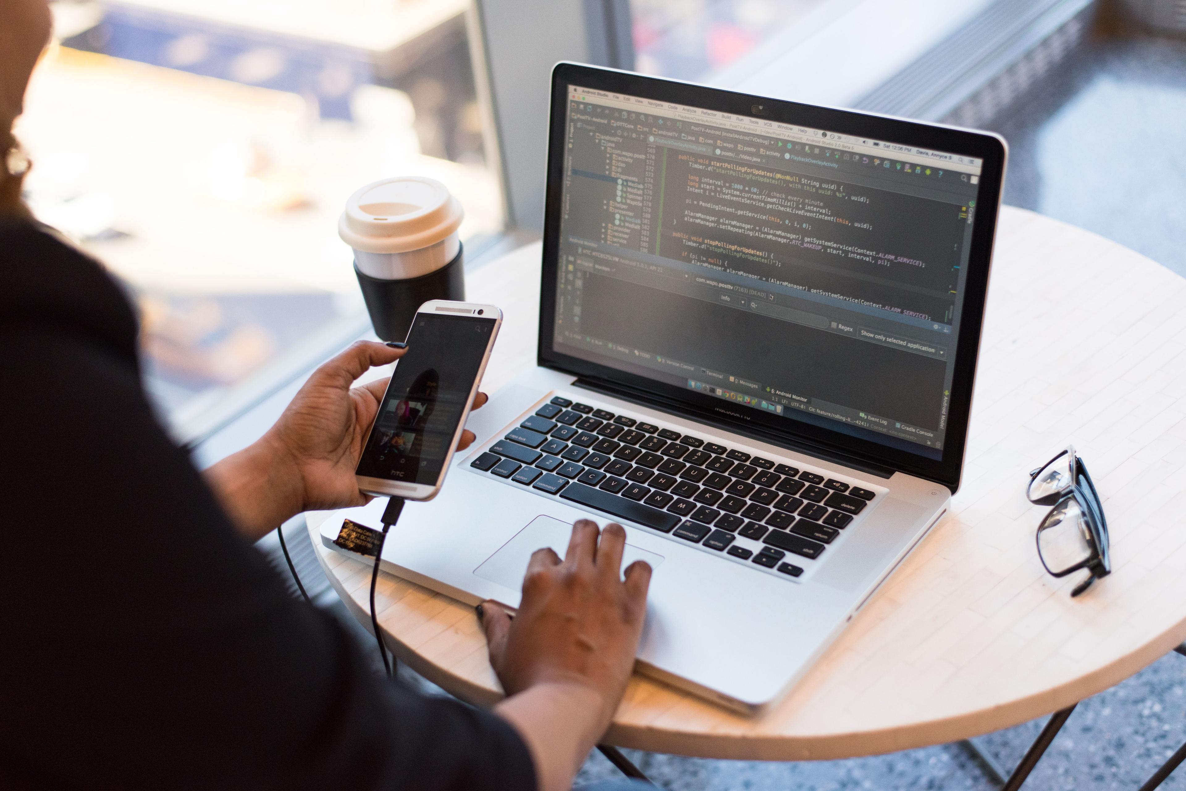 Developer working with smartphone and laptop on desk