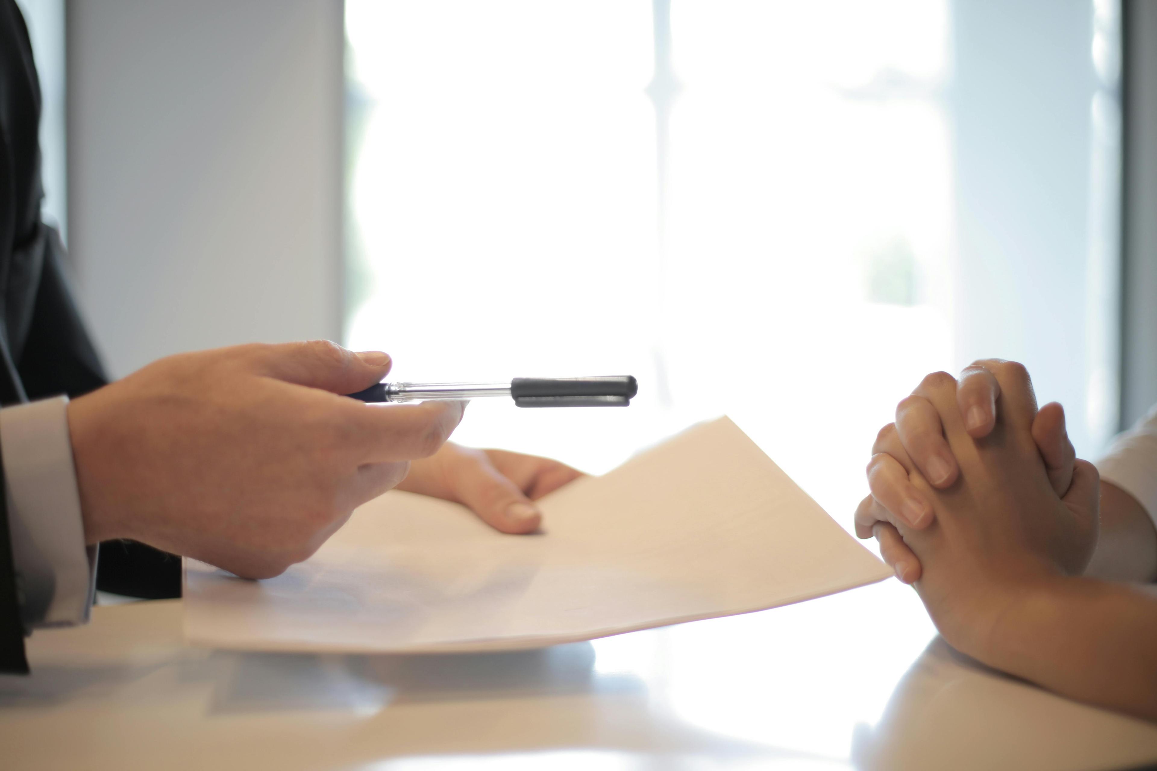Businessman extending a contract document for signature across a desk