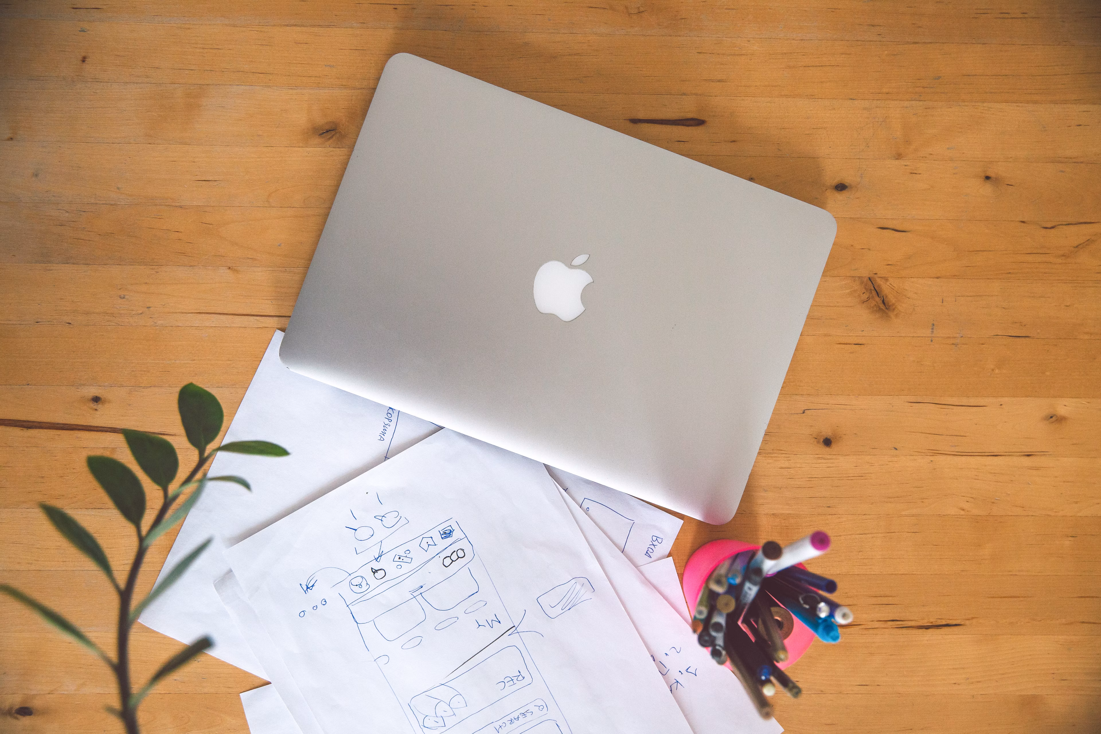 Top view of laptop papers and pens on a wooden table in an office setting