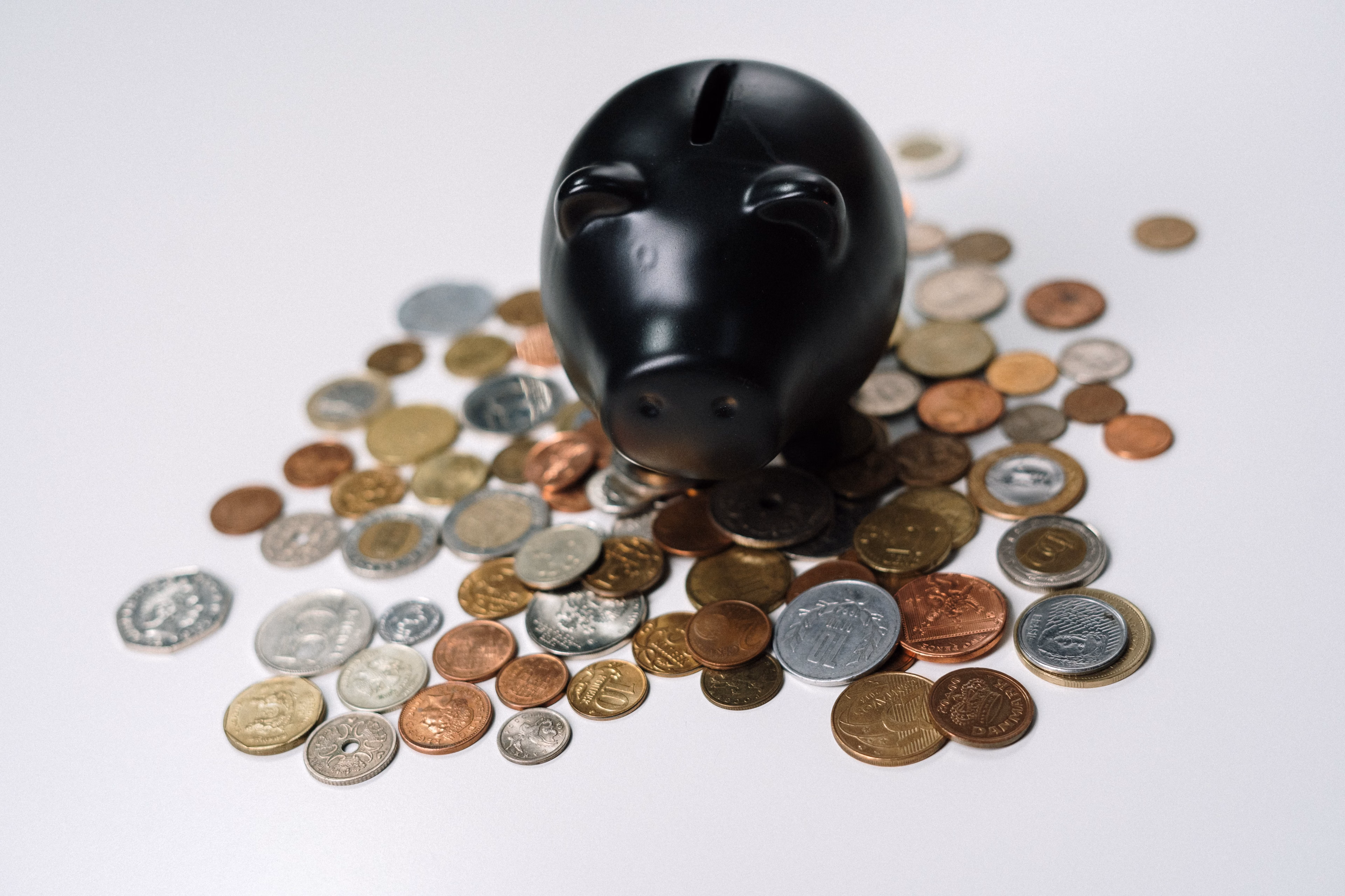 Black piggy bank surrounded by a variety of coins on a white surface