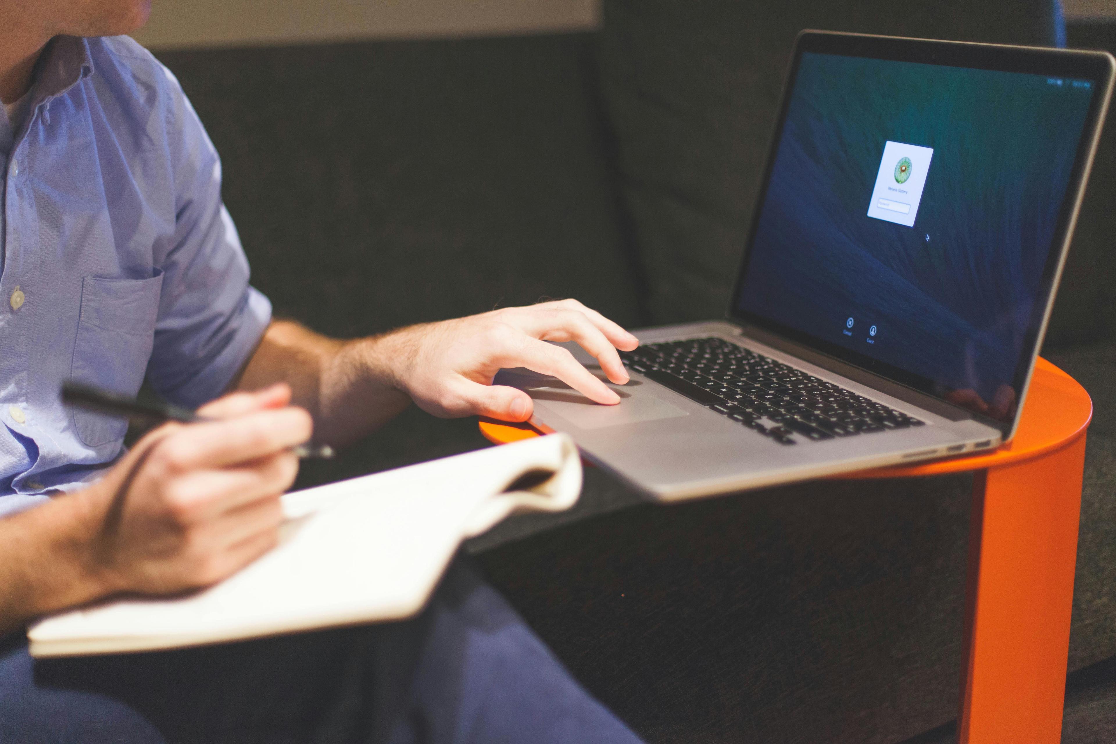 Developer writing notes beside an open laptop at their desk
