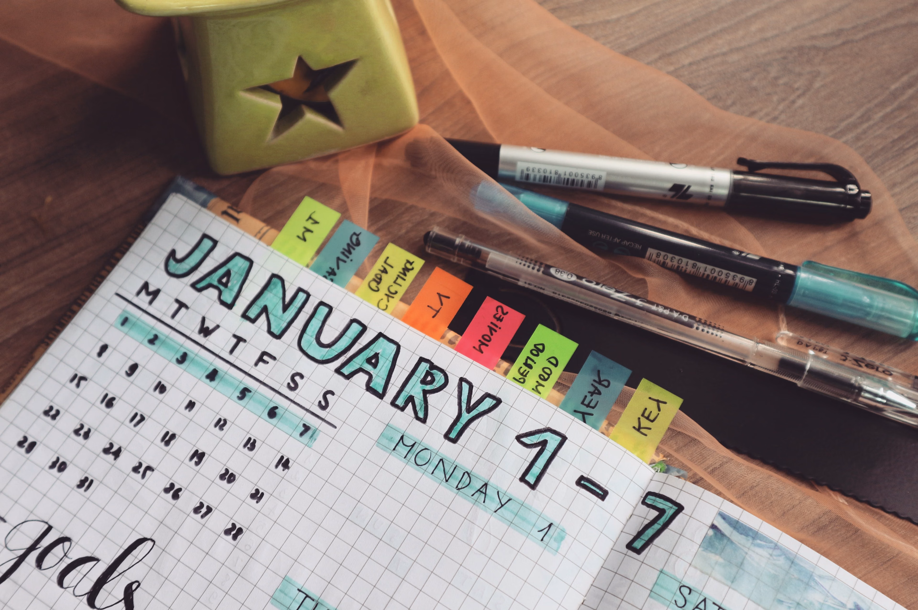Detailed planner with goals and colorful tabs on a wooden desk with pens