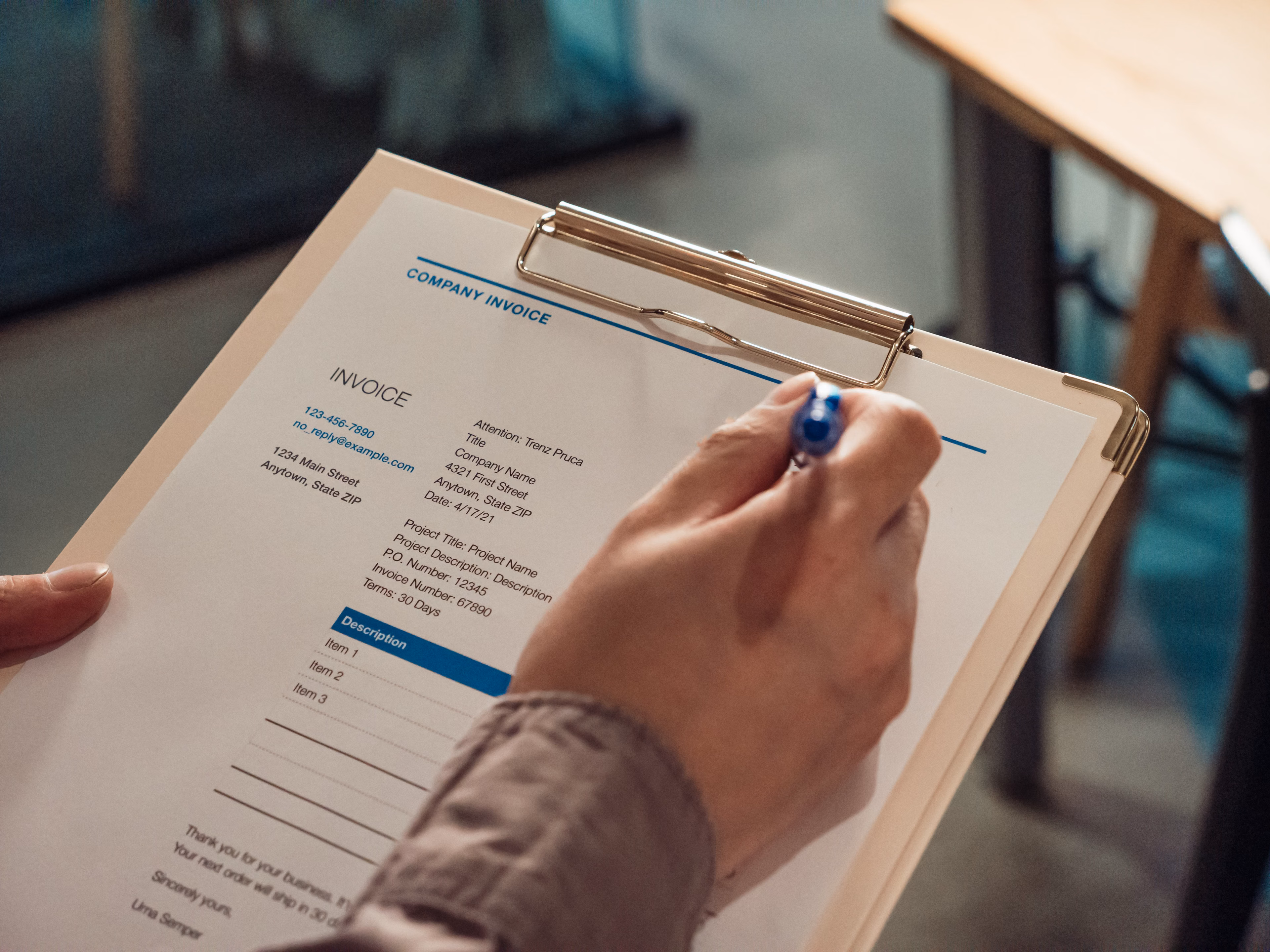 Hand holding a company invoice on a clipboard with a pen