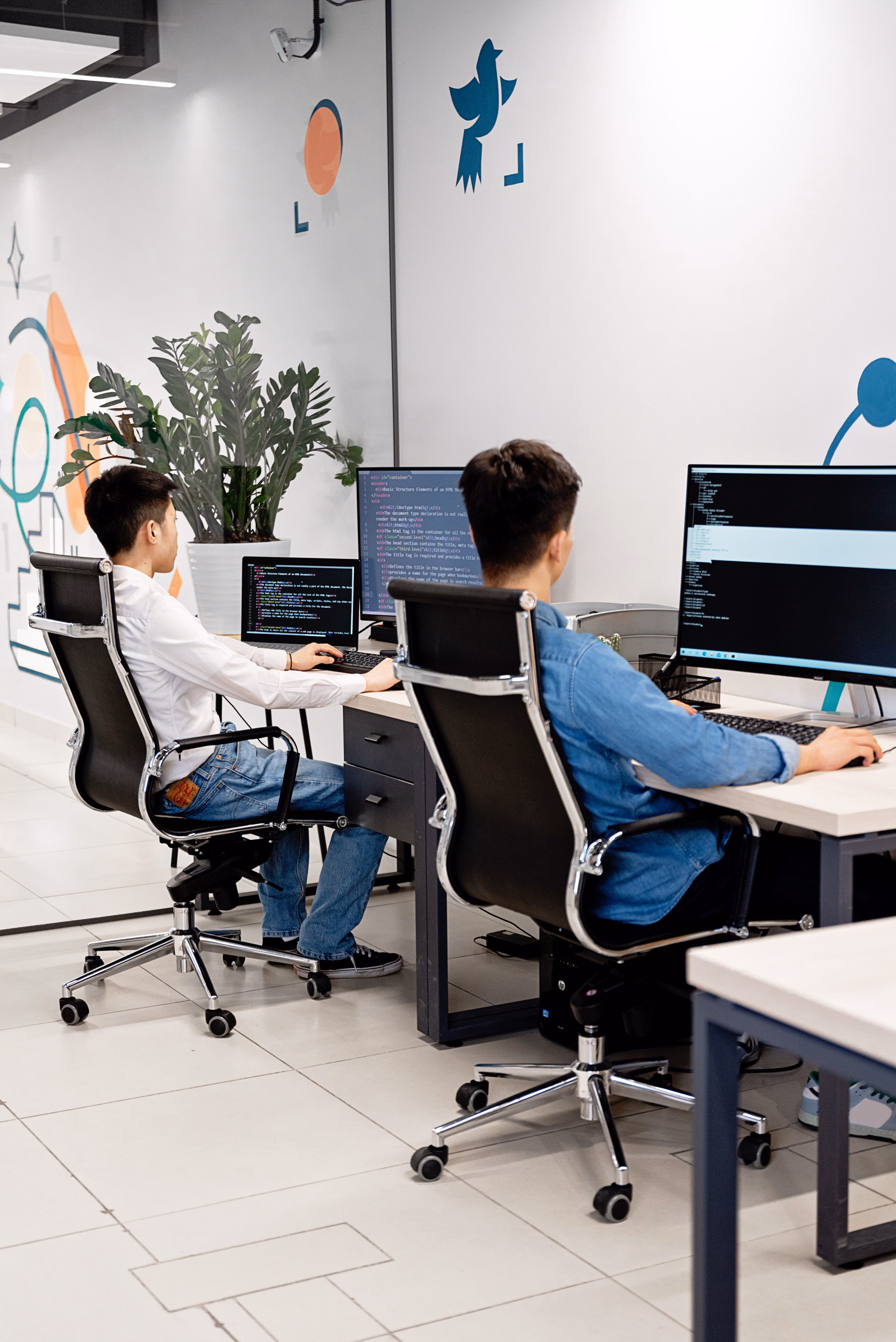 Two programmers collaborating in a bright modern office while coding on monitors