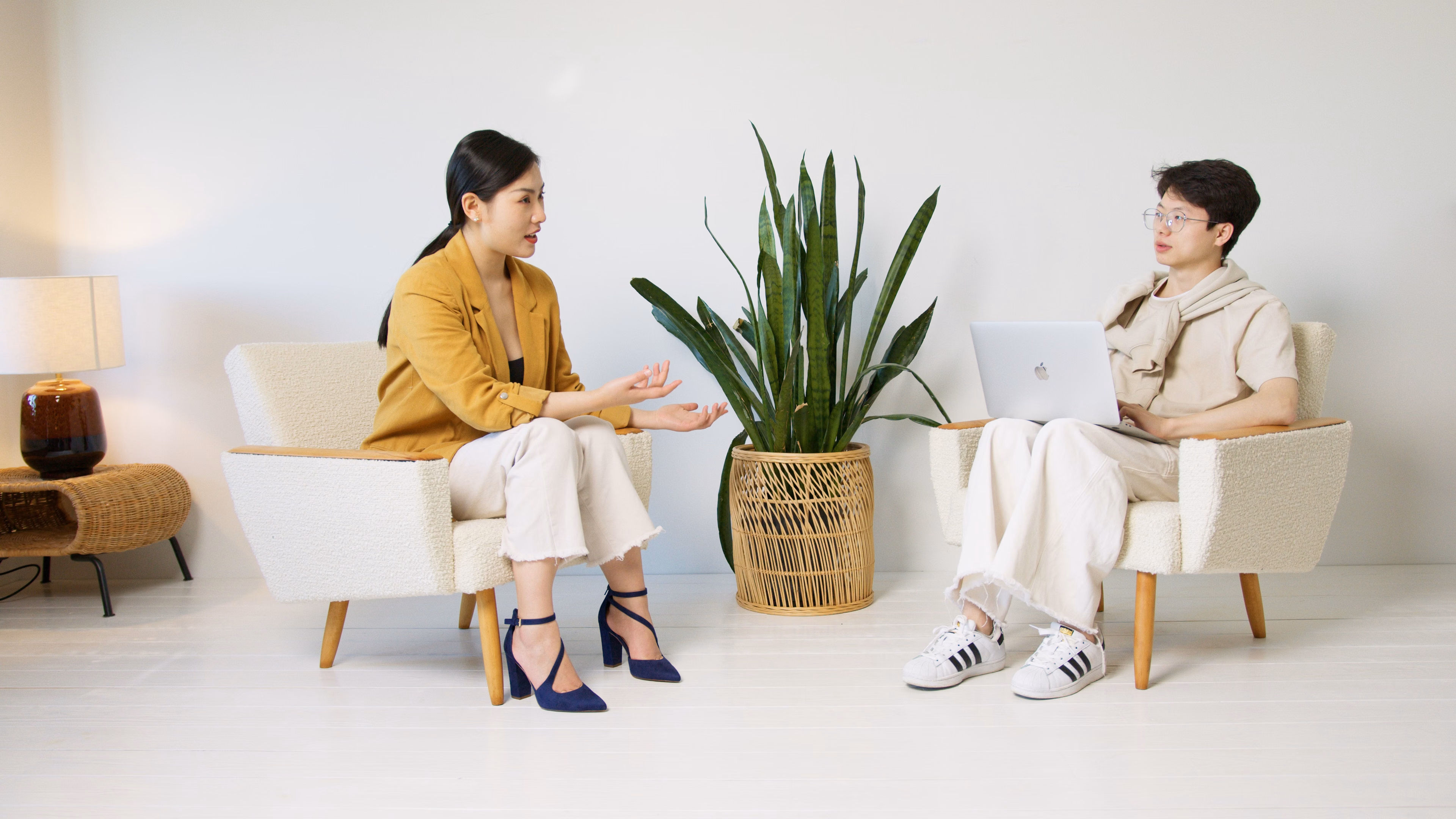 Two people having a casual interview conversation indoors with minimalist decor and a houseplant